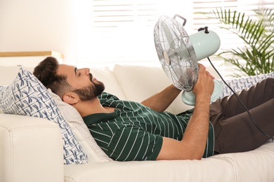 Photo of Man with fan enjoying air flow at home. Summer heat