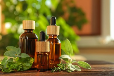 Bottles of essential oil and fresh herbs on wooden table in room. Space for text