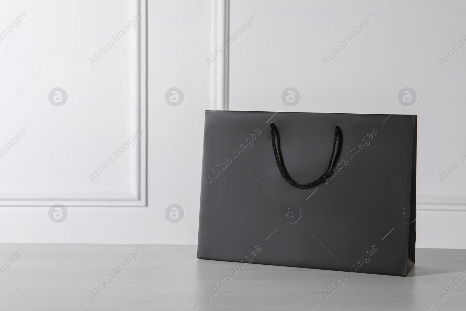 Photo of Black paper bag on white wooden table, space for text