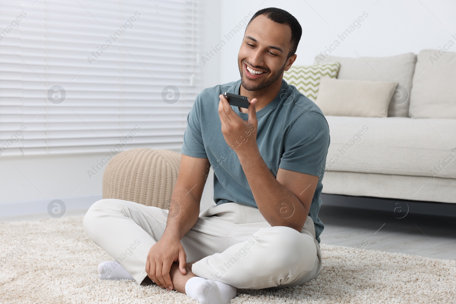 Photo of Happy man sending voice message via smartphone indoors