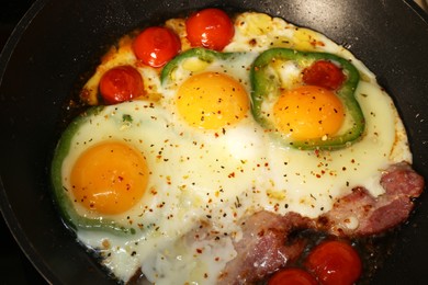 Photo of Cooking eggs with bacon, tomatoes and pepper in frying pan, closeup