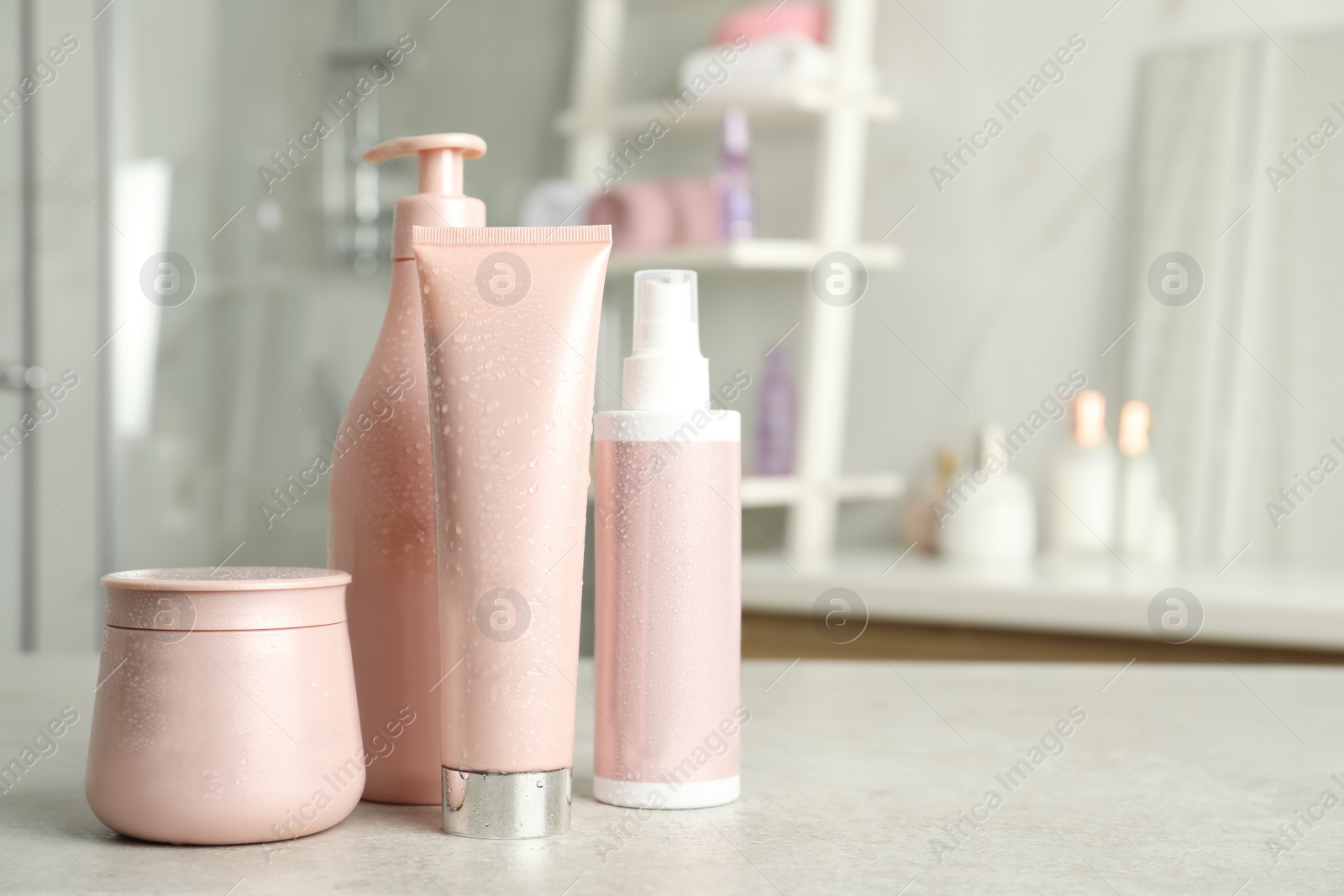 Photo of Set of hair care cosmetic products covered with water drops on light grey stone table in bathroom. Space for text