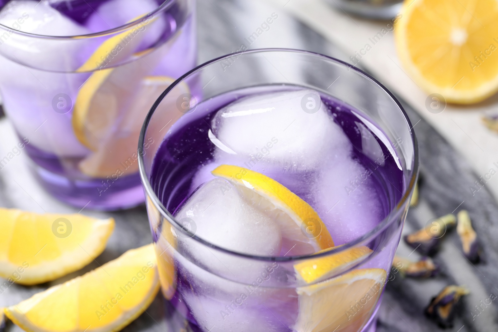 Photo of Organic blue Anchan with lemon and ice cubes on table, closeup. Herbal tea