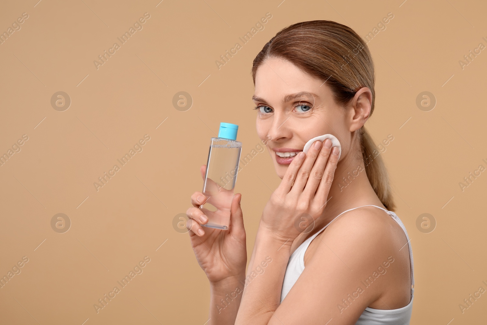 Photo of Beautiful woman removing makeup with cotton pad on beige background, space for text