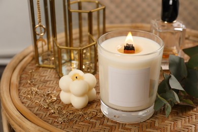 Burning soy candle, perfume and stylish accessories on wicker table indoors