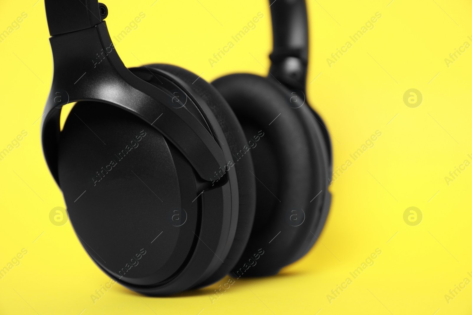 Photo of Modern wireless headphones on yellow background, closeup. Space for text