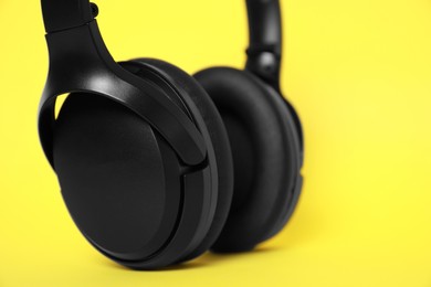 Photo of Modern wireless headphones on yellow background, closeup. Space for text