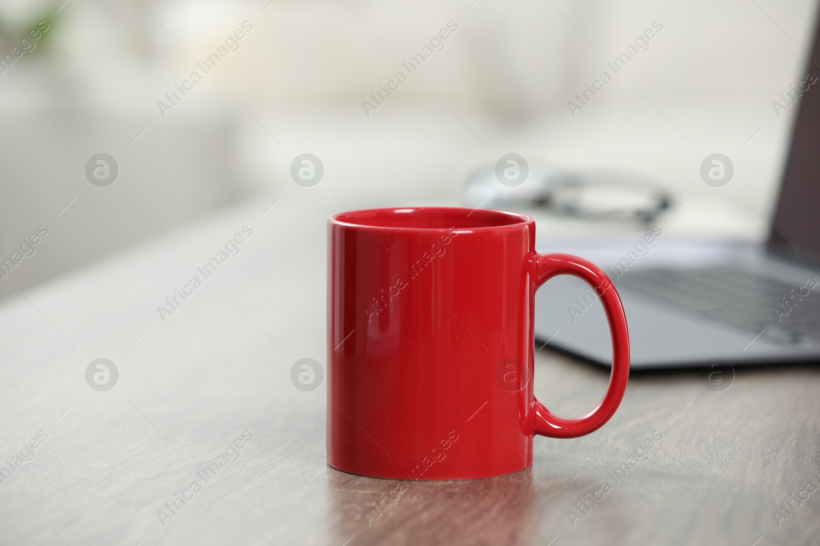 Photo of Red ceramic mug and laptop on wooden table indoors