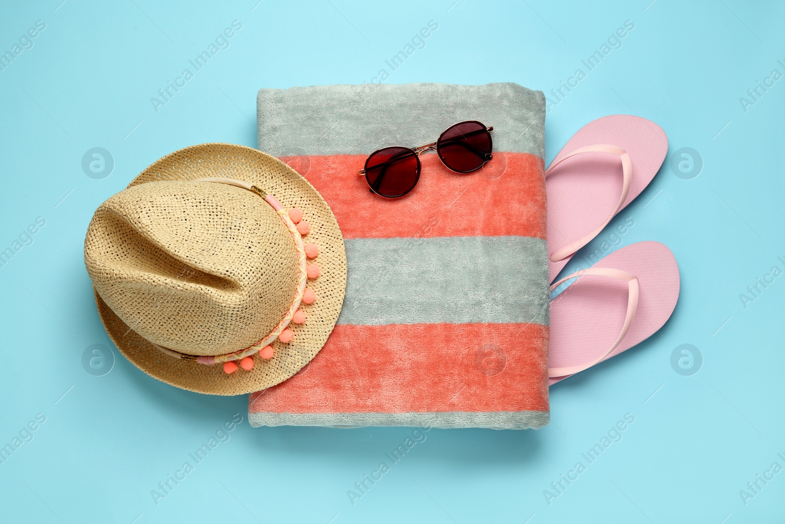 Photo of Beach towel, flip flops, straw hat and sunglasses on light blue background, flat lay