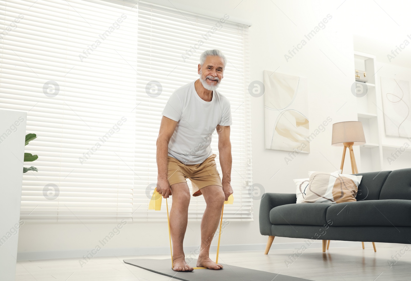 Photo of Senior man doing exercise with fitness elastic band on mat at home