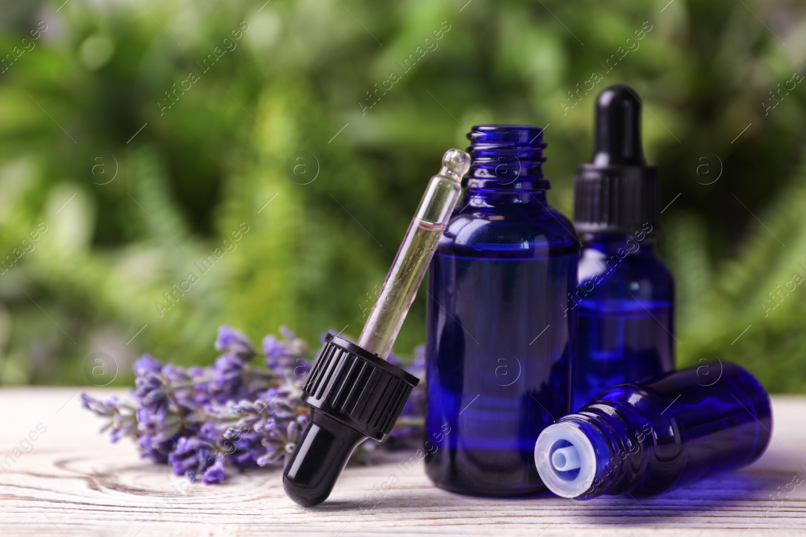 Photo of Bottles with natural lavender essential oil on white wooden table against blurred background. Space for text