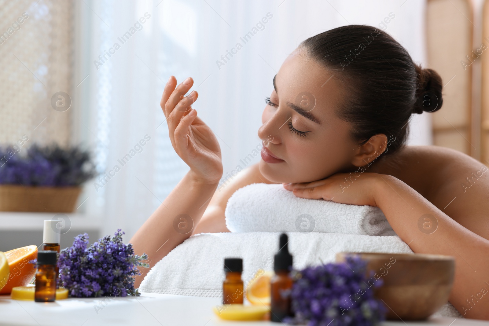 Photo of Beautiful young woman relaxing on massage couch and bottles of essential oil with ingredients on table in spa salon