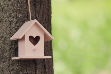 Photo of Pink bird house on tree trunk outdoors. Space for text