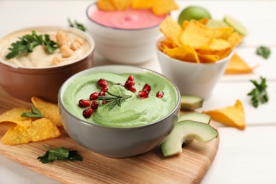 Bowl of delicious green hummus with rosemary and pomegranate seeds on white wooden table. Space for text