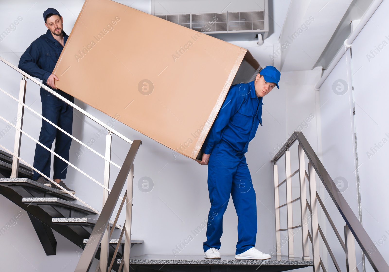 Photo of Professional workers carrying refrigerator on stairs indoors