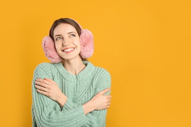 Happy woman wearing warm earmuffs on yellow background, space for text