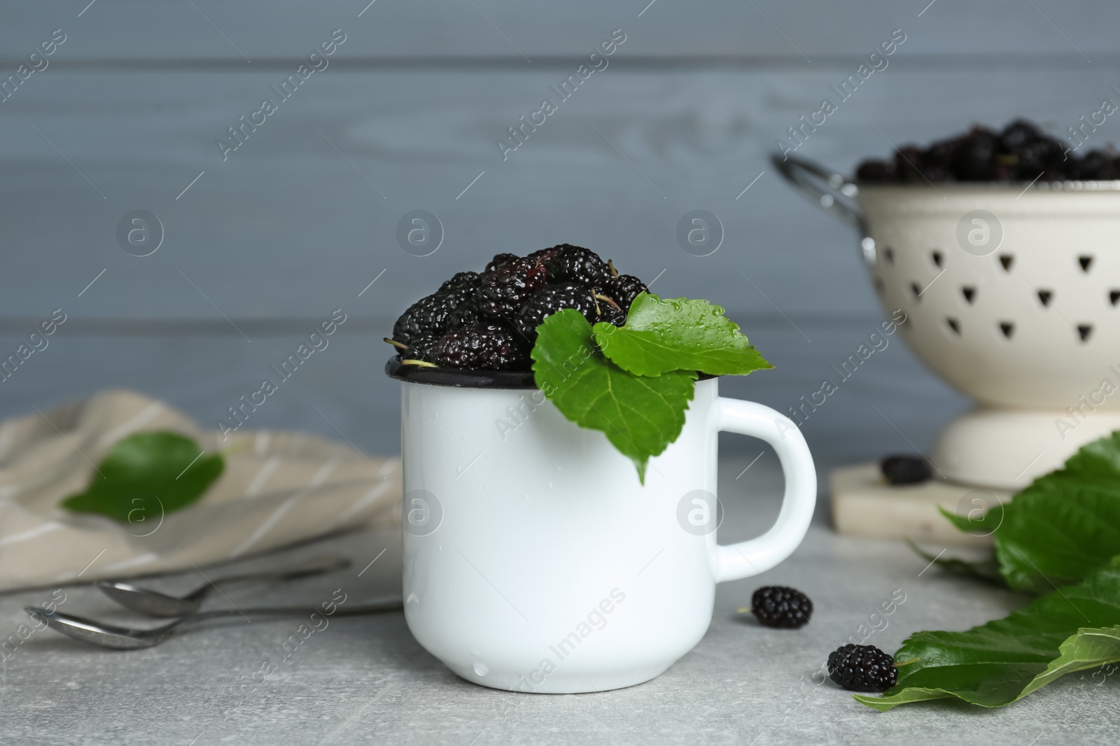 Photo of Cup of delicious ripe black mulberries on grey table