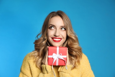 Happy young woman with Christmas gift on light blue background