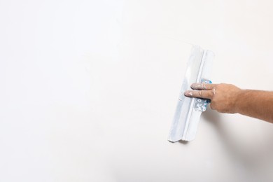 Photo of Worker plastering wall with putty knife indoors, closeup. Space for text