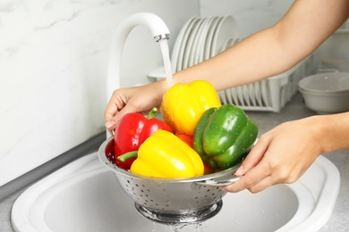 Photo of Woman washing paprika peppers in kitchen sink, closeup