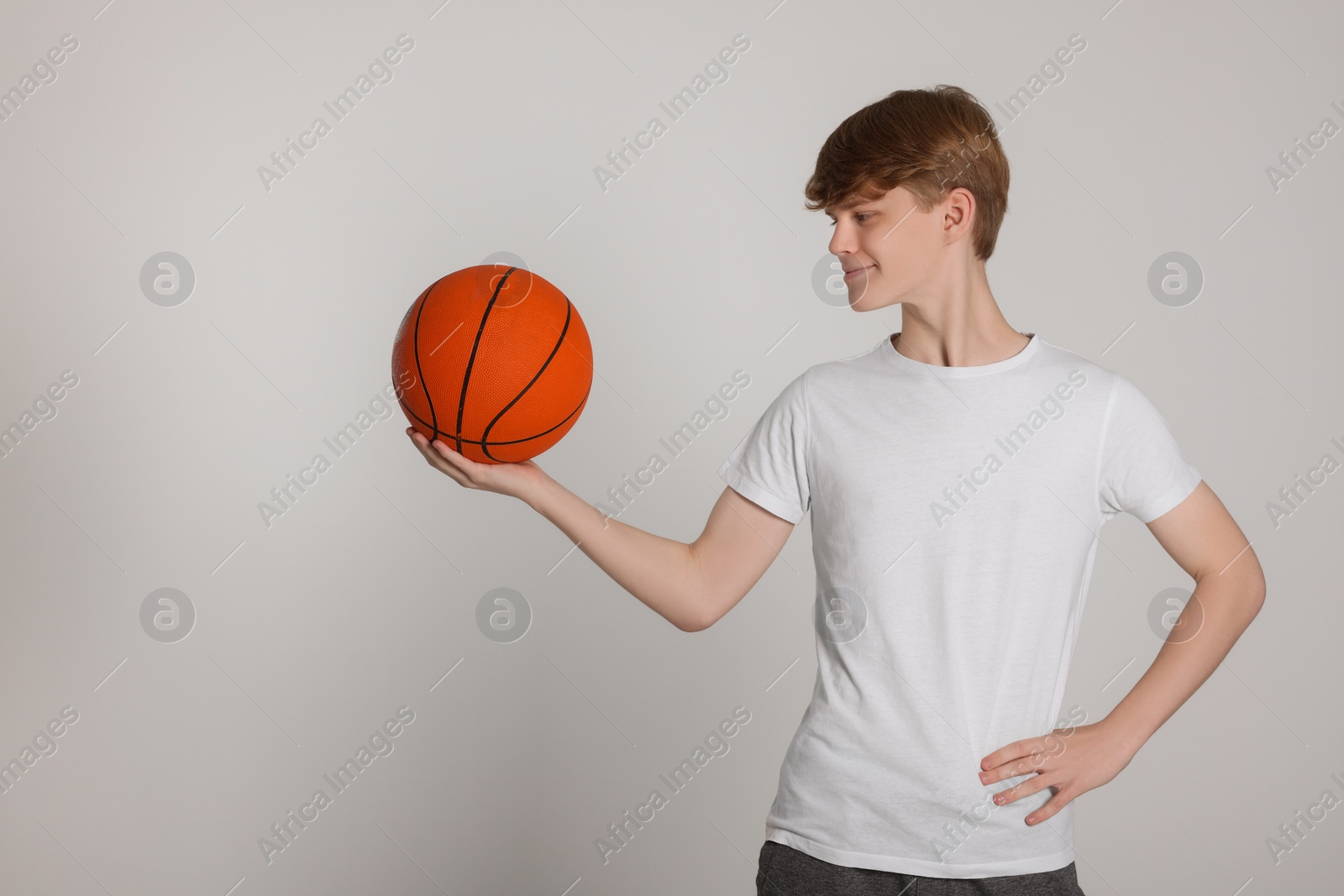 Photo of Teenage boy with basketball ball on light grey background. Space for text