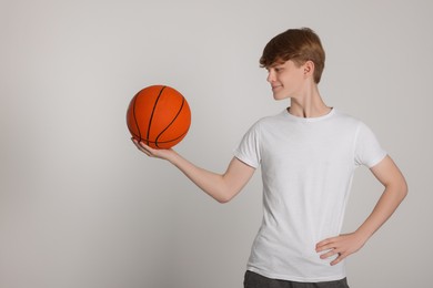 Photo of Teenage boy with basketball ball on light grey background. Space for text