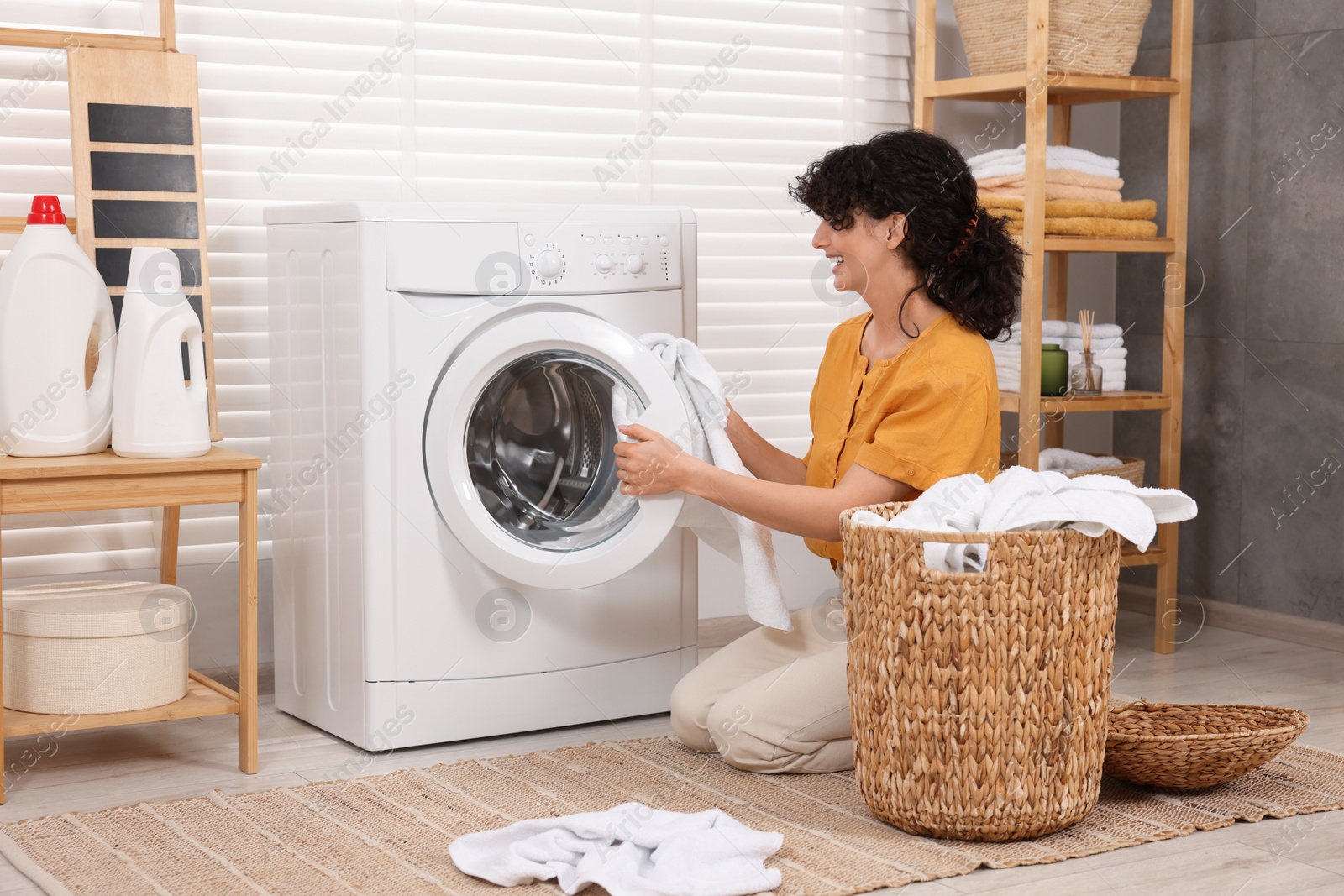 Photo of Happy woman putting laundry into washing machine indoors