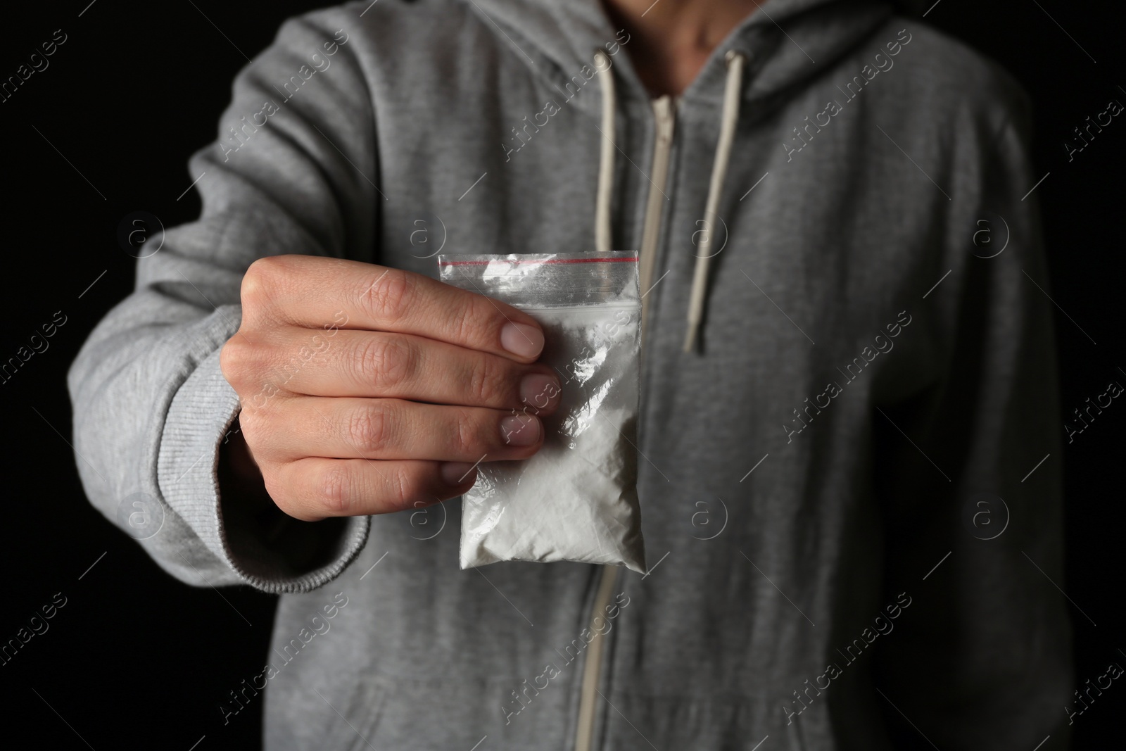 Photo of Drug dealer holding bag with cocaine on black background, closeup