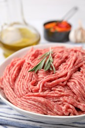 Fresh raw ground meat and rosemary in bowl on table, closeup