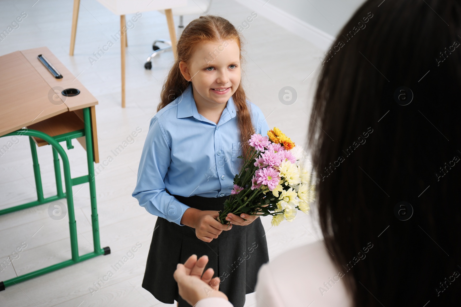 Photo of Schoolgirl with bouquet congratulating her pedagogue in classroom. Teacher's day