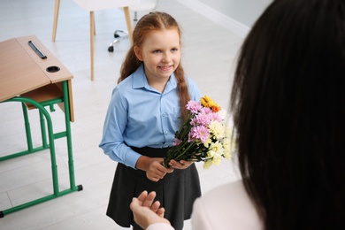 Photo of Schoolgirl with bouquet congratulating her pedagogue in classroom. Teacher's day