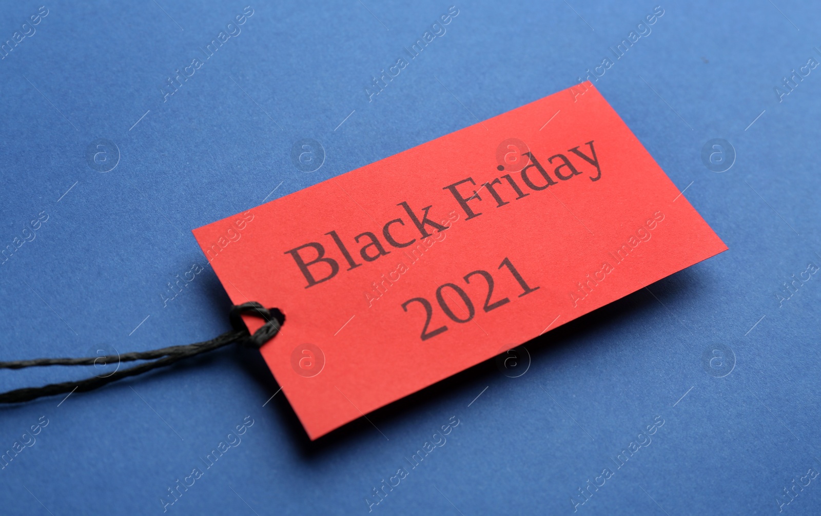 Photo of Red tag with words BLACK FRIDAY 2021 on blue background, closeup