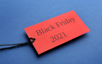 Red tag with words BLACK FRIDAY 2021 on blue background, closeup