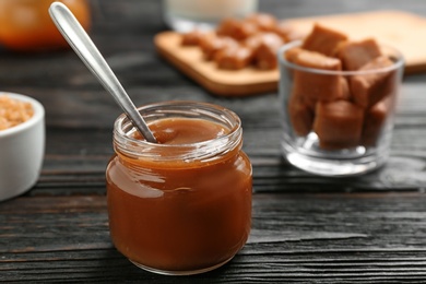 Jar with tasty caramel sauce and spoon on wooden table. Space for text