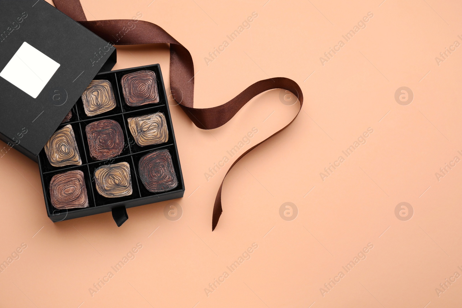 Photo of Box of tasty chocolate candies and ribbon on beige background, flat lay. Space for text