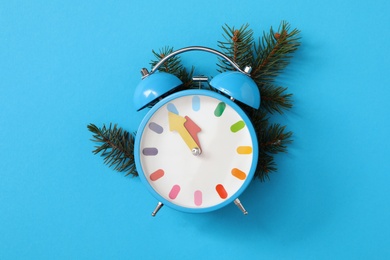 Alarm clock and fir branch on light blue background, flat lay. New Year countdown