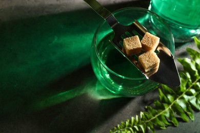 Photo of Absinthe in glass, spoon, brown sugar, and fern leaf on gray table, above view with space for text. Alcoholic drink