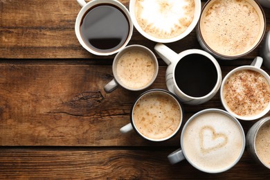 Many cups of different coffees on wooden table, flat lay. Space for text