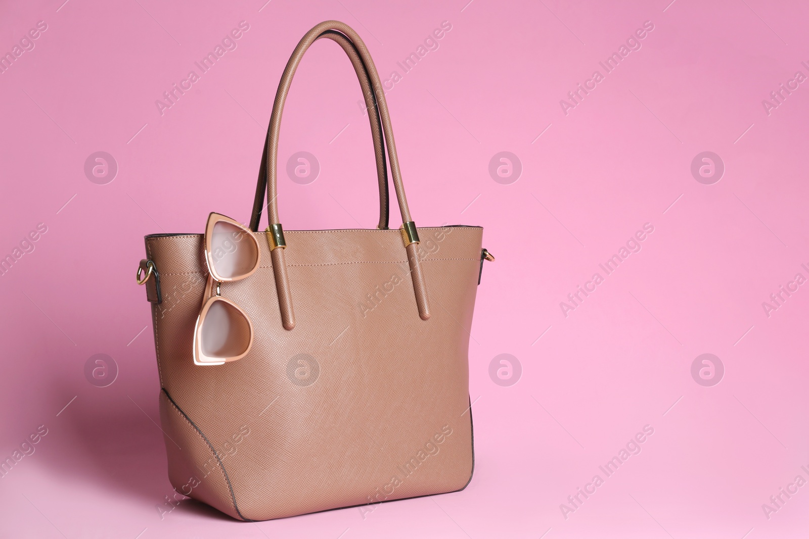 Photo of Stylish woman's bag and sunglasses on light pink background. Space for text