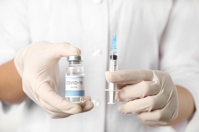 Doctor holding vial with vaccine and syringe against Covid-19, closeup