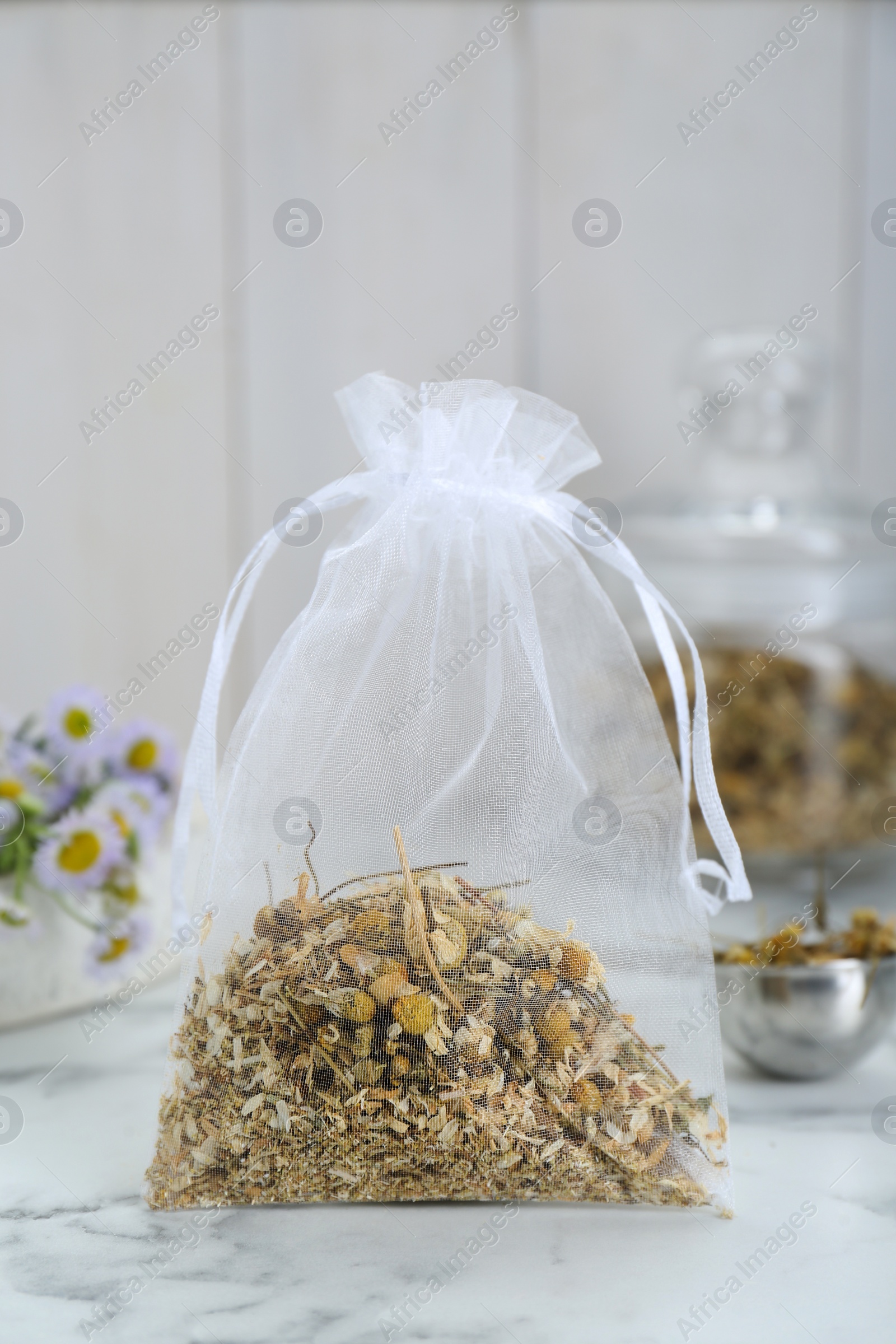Photo of Scented sachet with dried chamomile flowers on white marble table