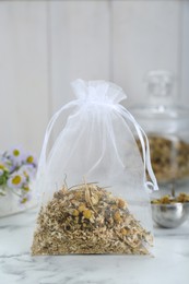 Photo of Scented sachet with dried chamomile flowers on white marble table