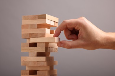 Photo of Playing Jenga. Man removing wooden block from tower on grey background, closeup