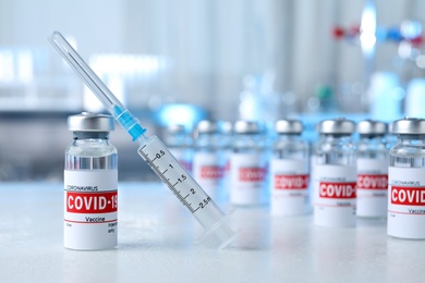Photo of Glass vial with COVID-19 vaccine and syringe on light table. Space for text