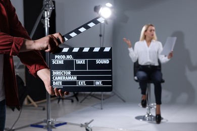 Photo of Casting call. Emotional woman performing while second assistance camera holding clapperboard against grey background in studio, selective focus