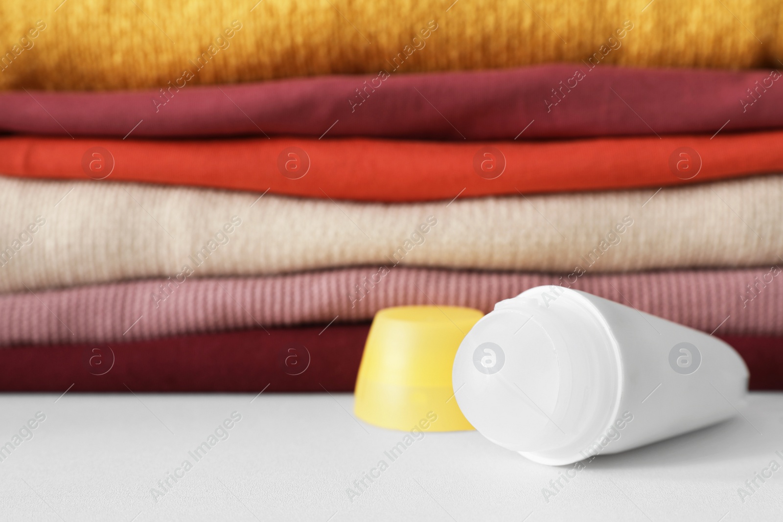 Photo of Roll-on deodorant near stack of clean clothes on white table