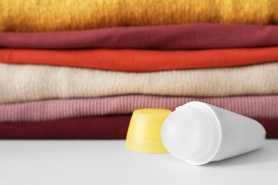 Photo of Roll-on deodorant near stack of clean clothes on white table