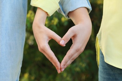 Photo of Couple making heart with hands outdoors on sunny day, closeup