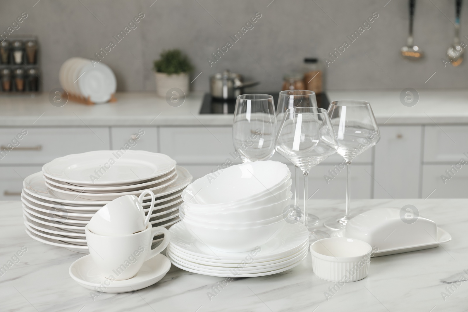 Photo of Clean plates, bowls, cups and glasses on white marble table in kitchen