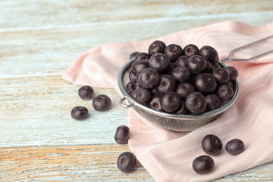 Photo of Metal sieve of fresh acai berries on light wooden table, closeup. Space for text